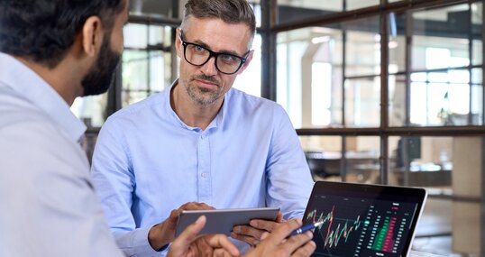 Diverse managers traders analysts discussing financial growth market at desk with laptop with graphs on screen using tablet device. Investors brokers analysing indexes online cryptocurrency stock