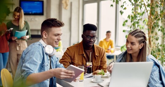 University students using laptop while going through lecture during lunch break in cafeteria.