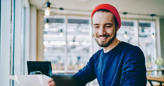 Caucasian male student connected to 4g for browsing internet on smartphone device during studying with textbook for education, successful hipster guy checking notification on cellular phone